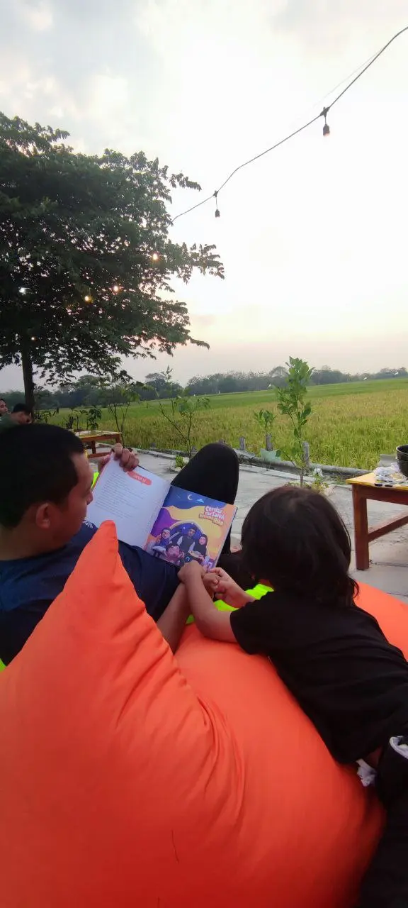 Ayah dan anak membaca buku bersama menjelang senja