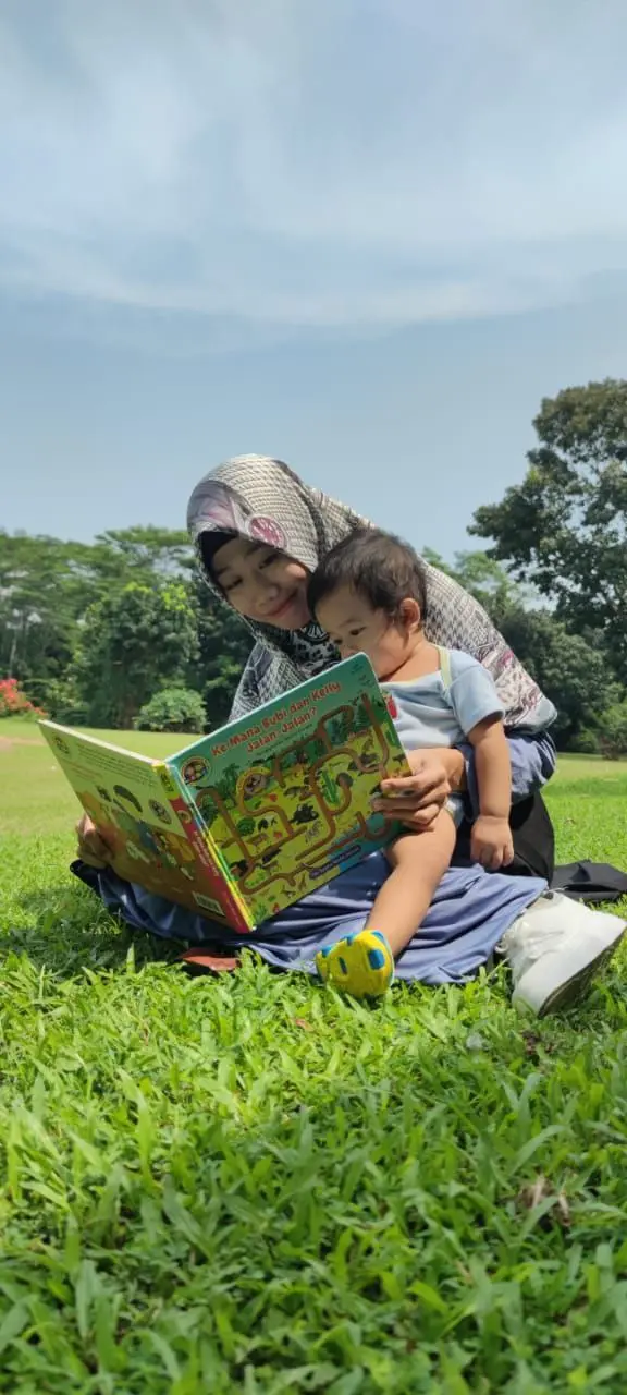 Ibu membaca buku bersama anak di taman