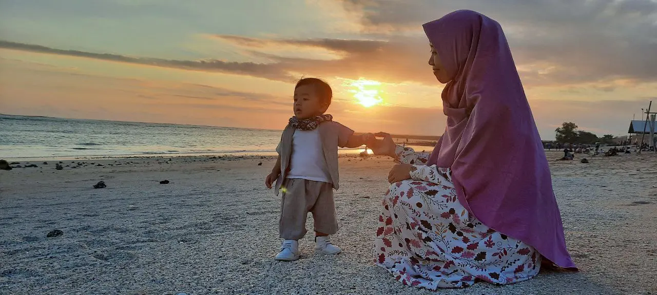 Ibu dan anak menikmati senja di tepi pantai